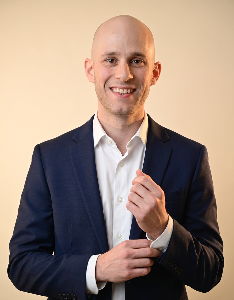 David Fink in a navy tailored jacket adjusting his cuff