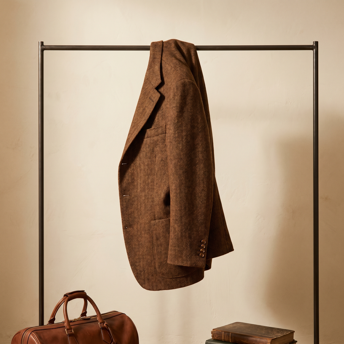 Brown herringbone tweed sport coat on a rack with a leather weekender bag