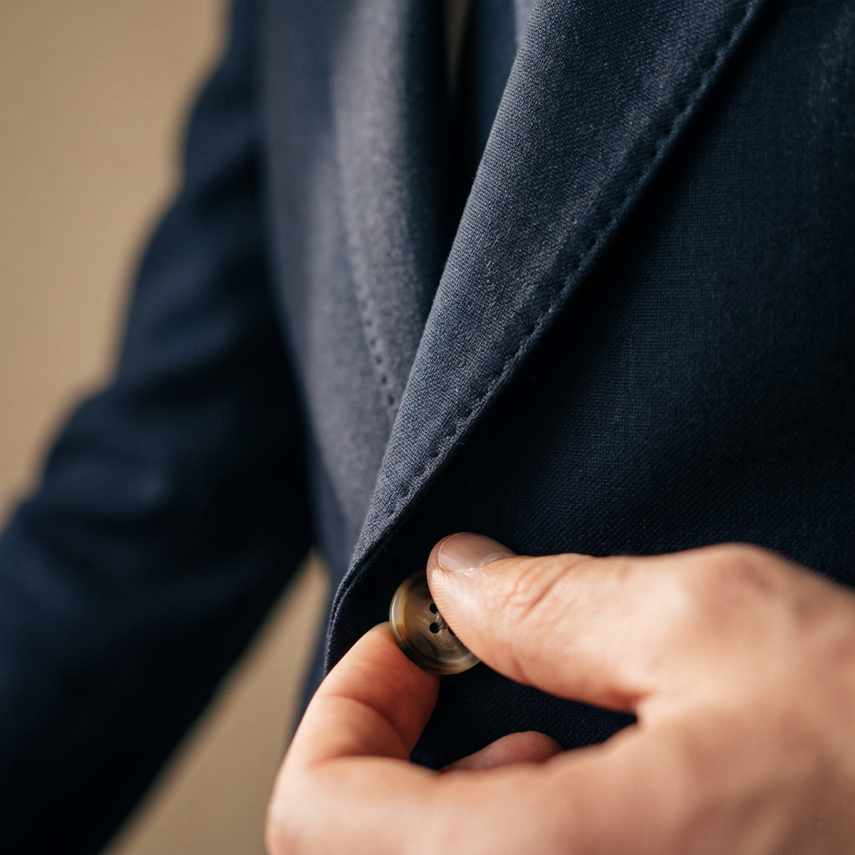 Hand fastening a horn button on a navy jacket with pick-stitched lapel