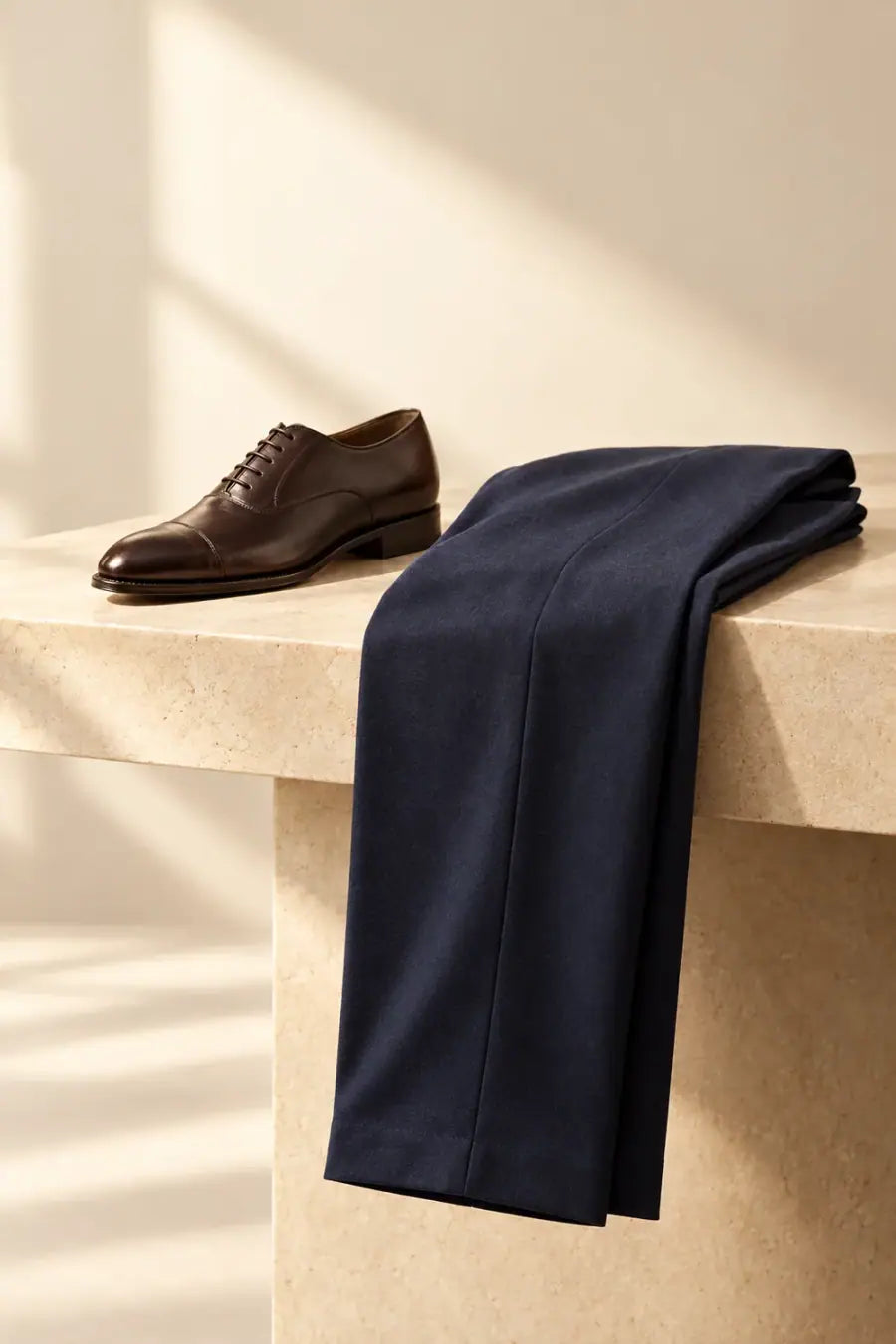 Folded navy tailored trousers beside a brown leather dress shoe